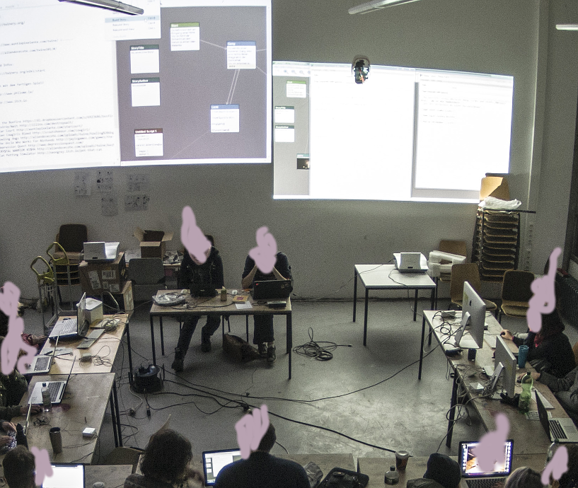 a group of people sitting in a workshop. their faces are blurred over. on the wall there are two large projections with twine-projects in the making